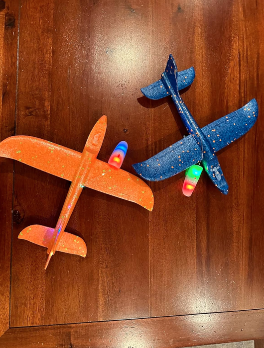 Two foam toy airplanes with LED lights, one orange and one blue, placed on a wooden surface, featured in a shopping article