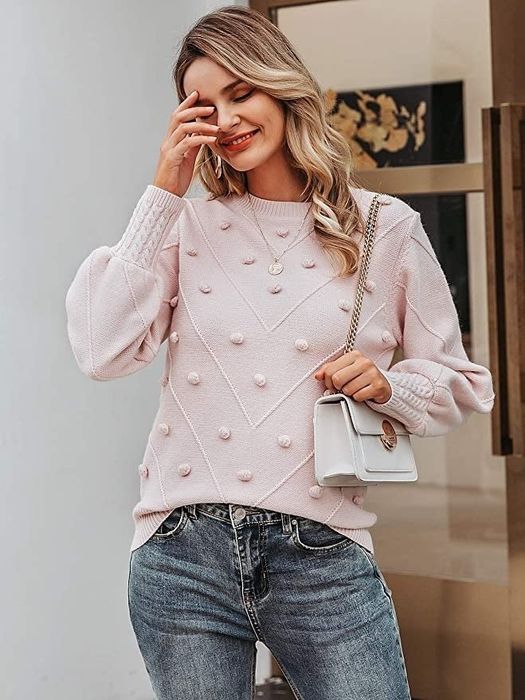 A model wearing a light pink sweater adorned with pom-poms throughout the design.