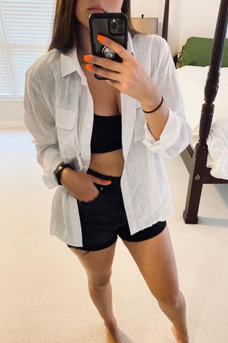 a selfie of a reviewer wearing the white shirt open over a black sports bra paired with shorts