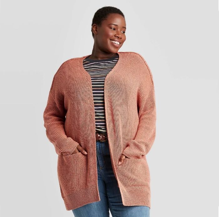 A model dons an orange cardigan over a striped shirt and jeans.