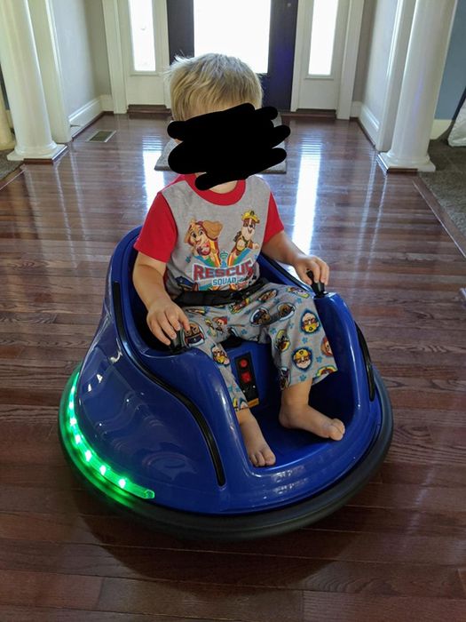 A child enjoys a ride in the blue bumper car, surrounded by green lights glowing from the base