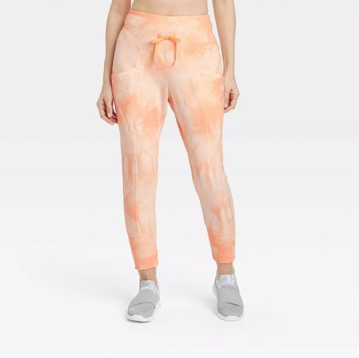 A model is sporting orange tie-dye joggers, paired with gray sneakers.