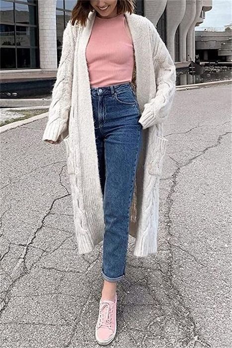 A model in a long white knit cardigan layered over a pink tee, combined with blue jeans and pink sneakers.