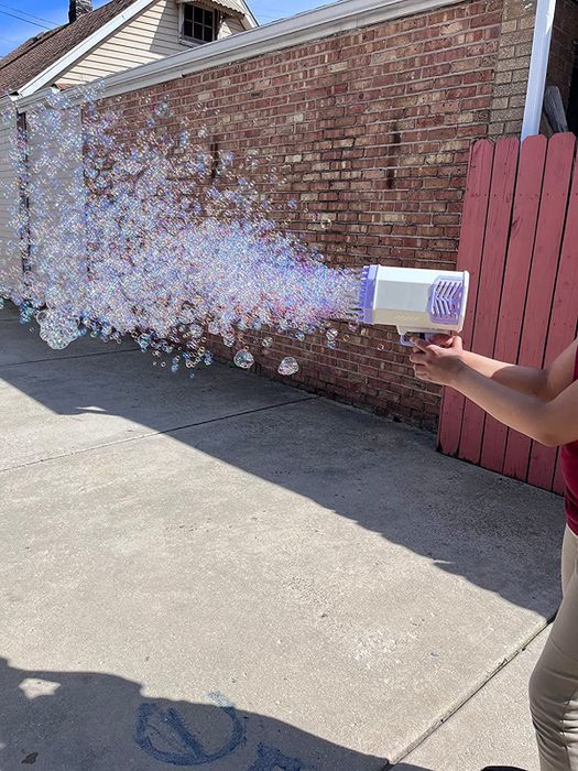 A reviewer using a bubble gun, with bubbles shooting everywhere