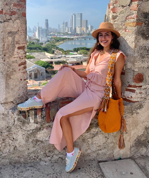 a reviewer wearing a pink top and pants, sitting in an old building with a city skyline in the backdrop