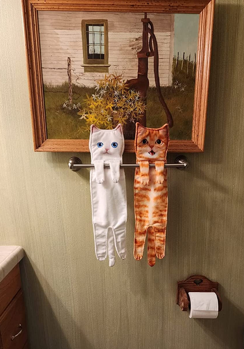 a white cat towel and an orange cat towel draped on a reviewer's towel rack