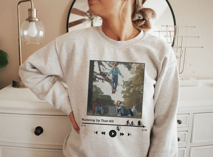 a model wearing the sweatshirt that looks like a song playing on a music streaming device with the cover art being an illustrated still of the television series scene