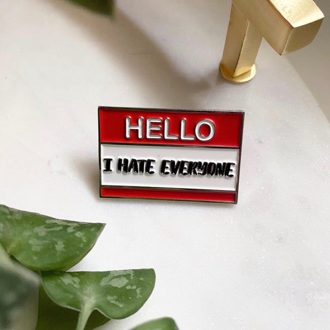 a red pin that reads ‘hello i hate everyone’, designed like a name tag