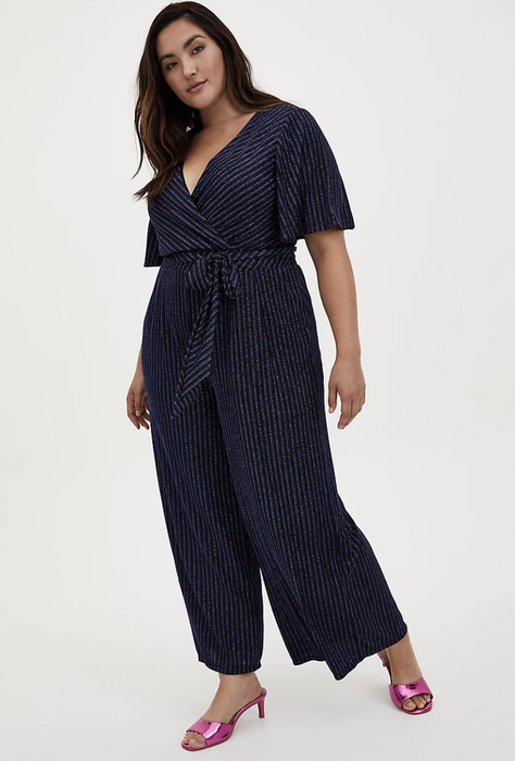 The model is wearing a Torrid jumpsuit paired with pink heels.