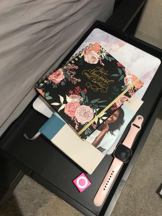 a reviewer photo showing the bedside caddy with an Apple Watch, iPod, notebooks, and a laptop