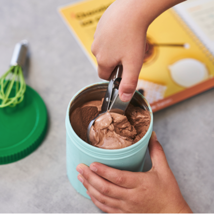 A hand scooping out creamy chocolate ice cream from a teal container