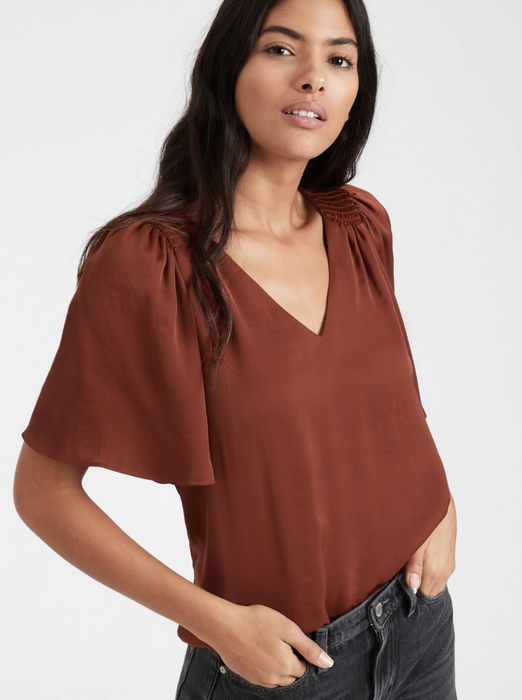The model is styled in a satin flutter-sleeve top in a warm burnt caramel brown.