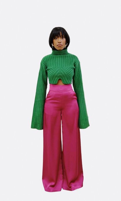 A model wearing a green ribbed cardigan with extra-long, wide sleeves, a notched cutout under the chest, and a turtleneck.