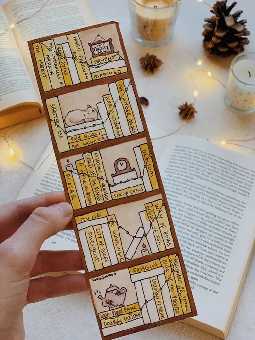 A hand holding a partially filled tracker bookmark over a book, ready to record the next title.