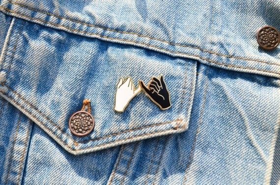 A pin depicting two hands, one white and one black, intertwining their pinky fingers as a symbol of unity and friendship.