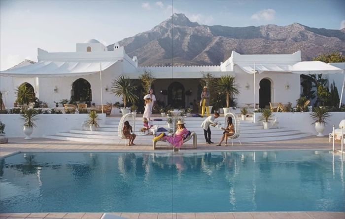 A two-page spread from the Slim Aarons book, featuring people lounging by a pool in luxurious egg chairs.