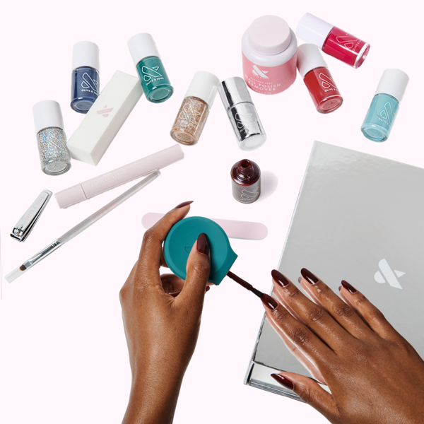 A model applying nail polish with a variety of nail products and polishes in the background, showing off the versatility of Olive and June's Mani System.