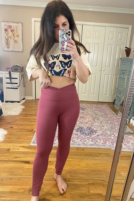 A reviewer is seen wearing pink criss-cross leggings paired with a butterfly cream oversized shirt, seated on a hardwood floor.