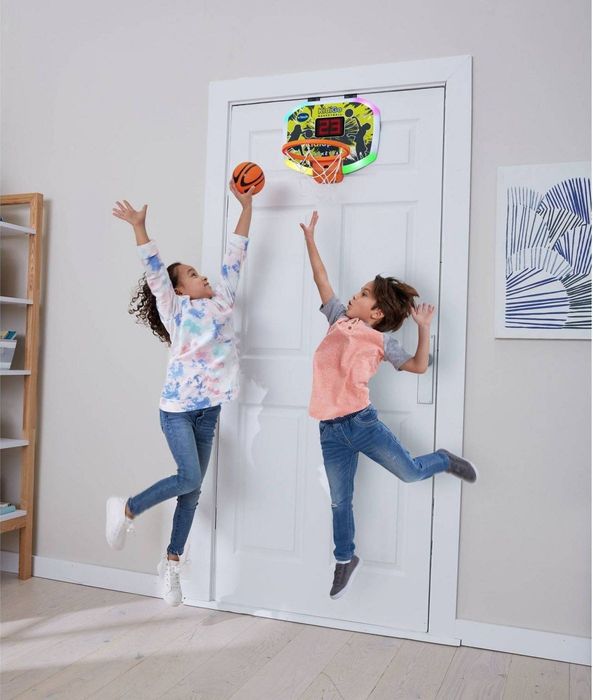 two children having a blast playing with the basketball hoop, which is mounted on the back of a door