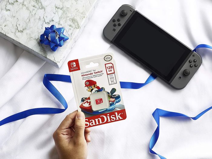 A hand holding a memory card in front of a Nintendo Switch