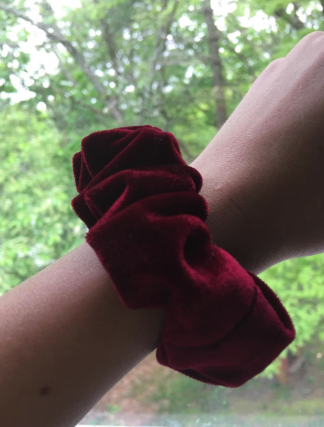 A reviewer's wrist adorned with a burgundy velvet scrunchie, adding a touch of elegance to their look.
