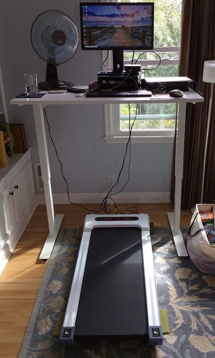 The white treadmill positioned neatly under a reviewer's standing desk setup.