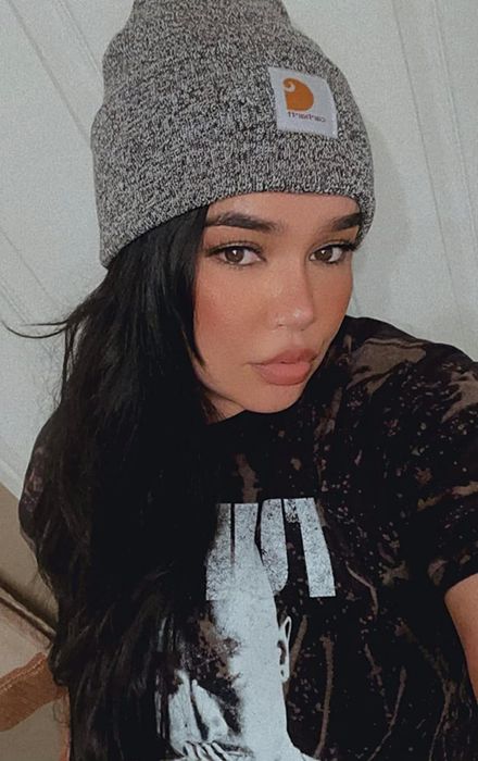 A reviewer modeling a grey Carhartt winter beanie.