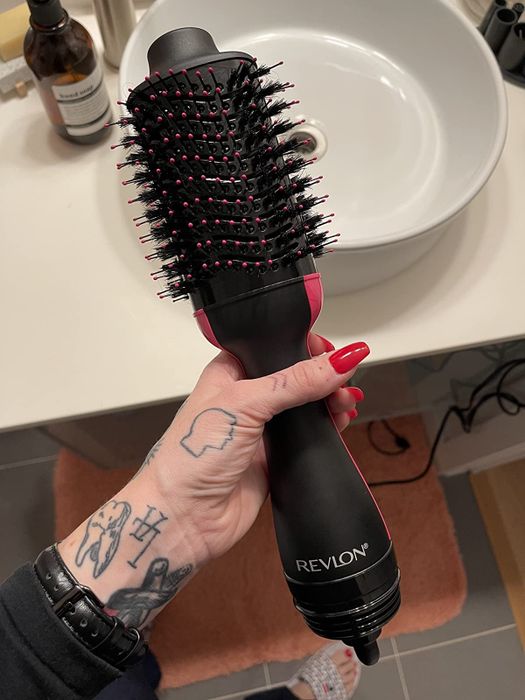 A reviewer holding the black and pink Revlon blow dry brush, ready to create sleek styles in no time.
