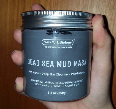 A reviewer holding a tub of gray Dead Sea mud mask.