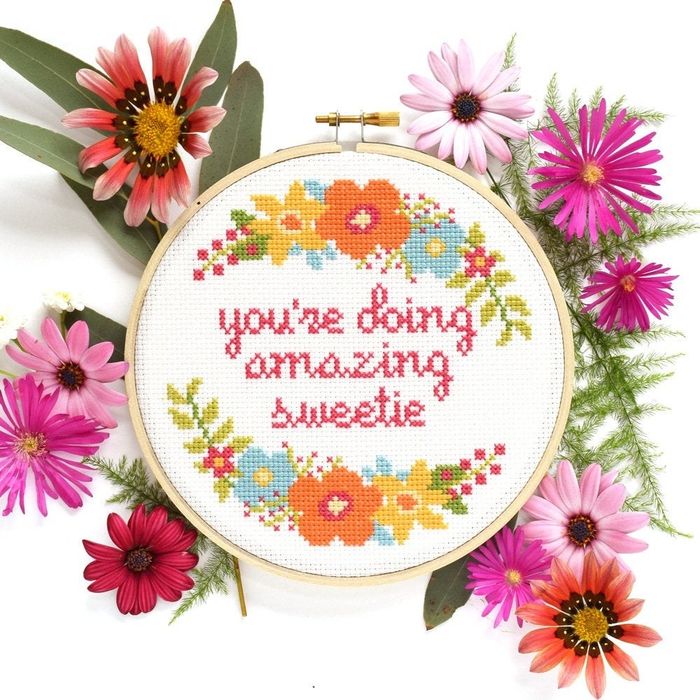 A cross-stitch displaying the words 'you're doing amazing sweetie' surrounded by flowers.