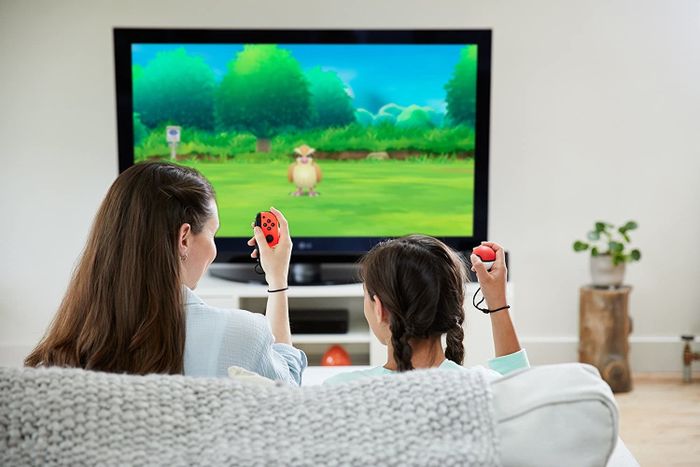 A young girl sitting on a couch while playing with the Poké Ball Plus.