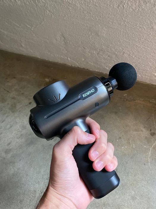A person holding the handle of a black massage gun.