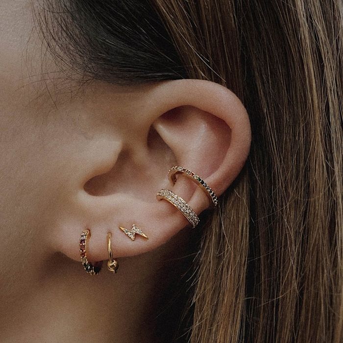 A model wearing a collection of earrings, including a delicate lightning bolt design.