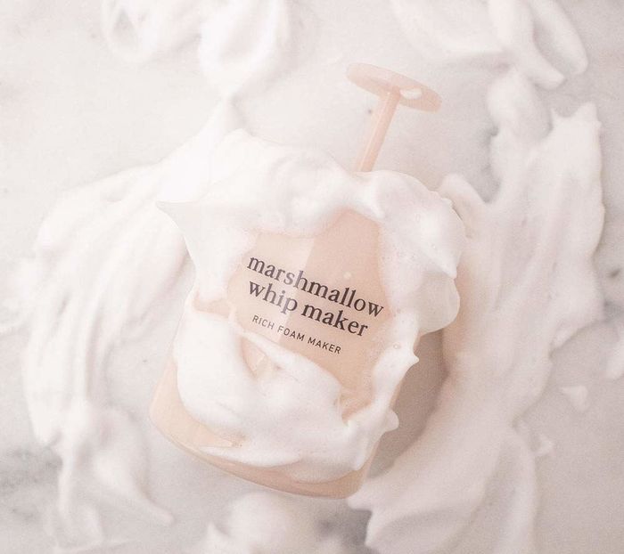 A pink container with a pump top for foaming the cleanser, surrounded by foamy cleanser.