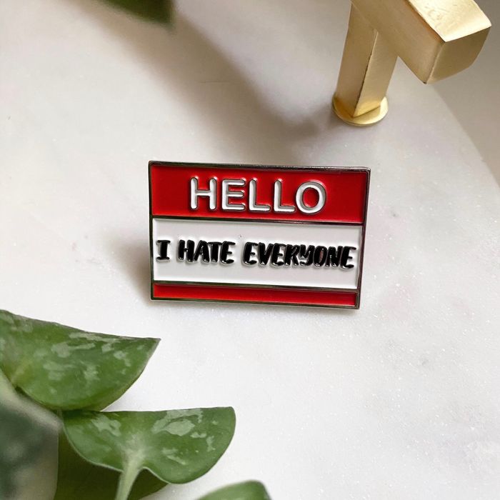 A red pin resembling a name tag with the phrase 'hello i hate everyone', capturing the essence of a rebellious mood.