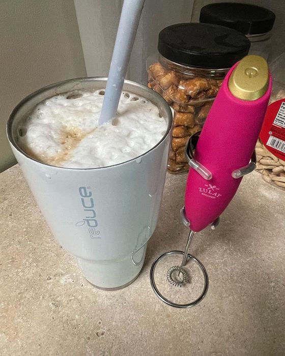 A pink milk frother placed next to a cup filled with frothy milk on top.