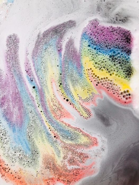 Rainbow-colored foam emerging from a cloud-shaped bath bomb, creating a magical, colorful display.