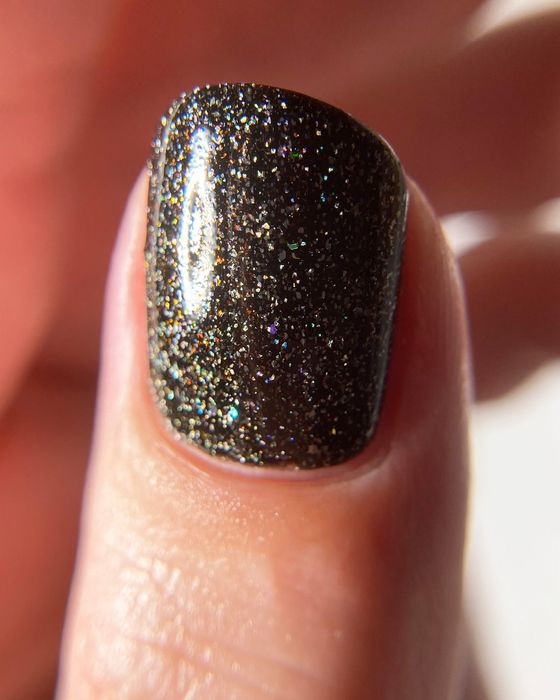 a thumb sporting a layer of black glittery nail polish