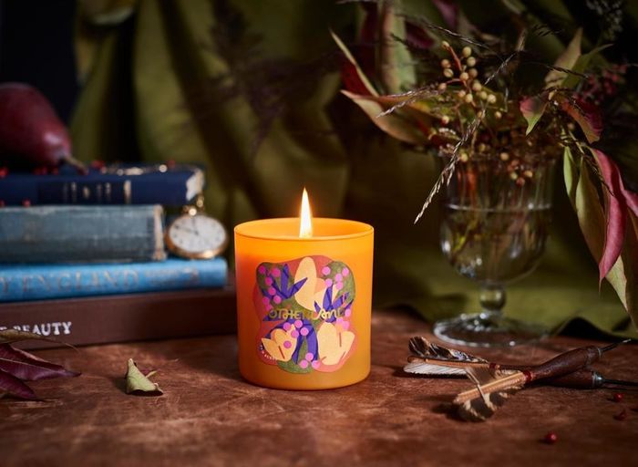 An orange candle with an artistic abstract label, perfect for adding a touch of elegance to any space.