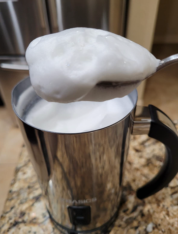 A silver frother with a spoon immersed in the frothed milk, showcasing its texture.