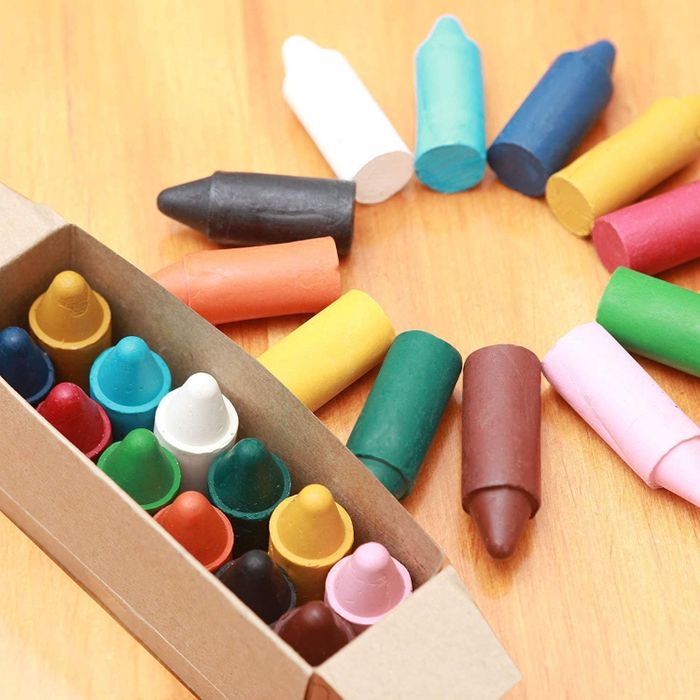 An open box of large, colorful crayons with some scattered in a circle on a table.