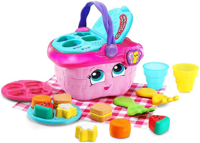 The pink picnic basket featuring a shape sorter lid and an assortment of pretend food and utensils.