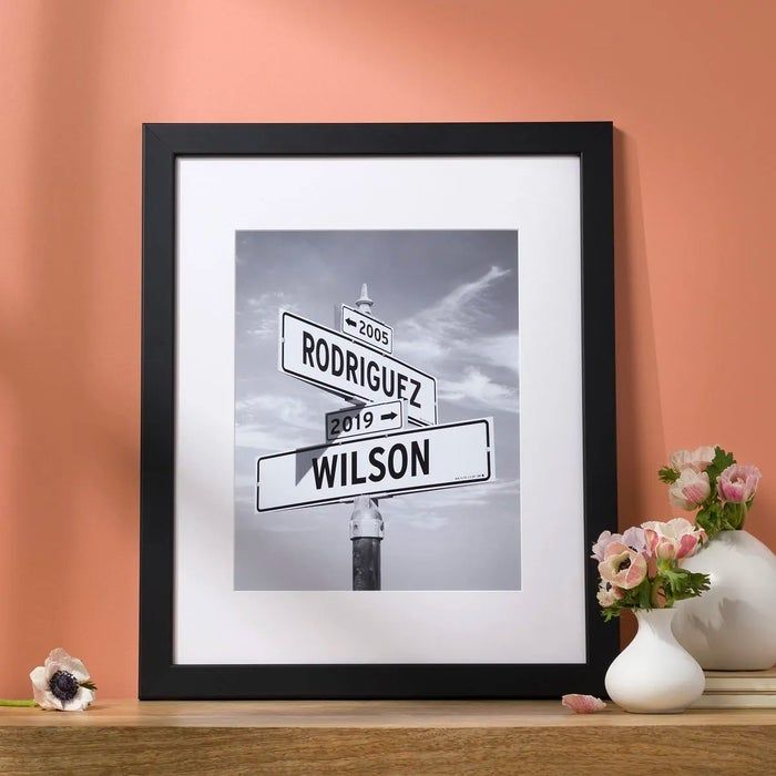 Framed black-and-white street signs displaying two last names and two years: one sign reads 'Rodriguez' and '2005', and the other reads 'Wilson' and '2019'.