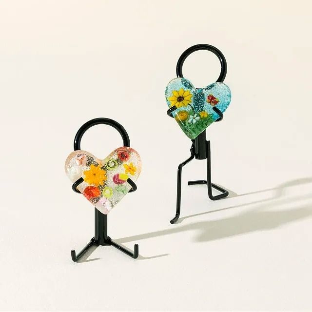 Two heart-shaped glass figurines with floral designs and metal stands, positioned as though walking.