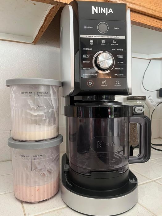 The Ninja ice cream maker sitting on a kitchen counter, accompanied by two containers filled with homemade ice cream.