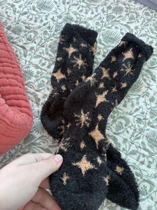 A pair of cozy black socks with star patterns, held in hand, resting on a patterned fabric.