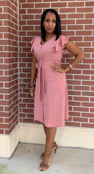 A reviewer sporting a knee-length pink dress with ruffle sleeves.