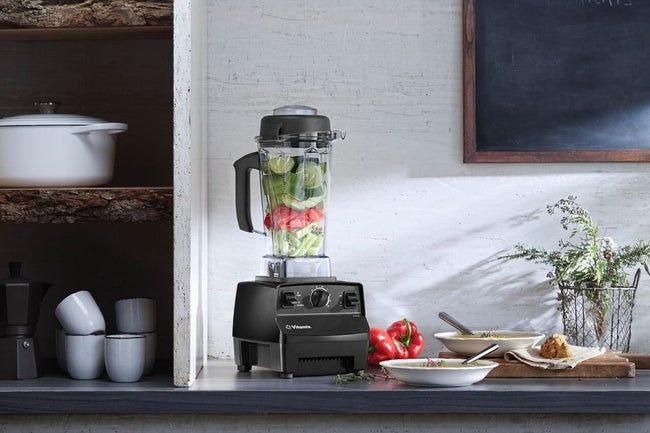 A large Vitamix blender filled with fresh vegetables, sitting on a kitchen countertop.