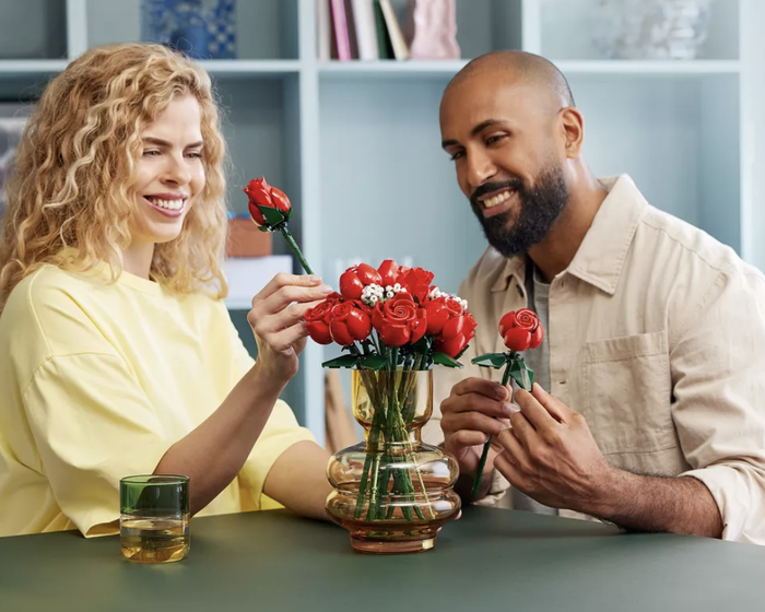A couple assembles a bouquet of LEGO roses inside a glass vase, smiling and enjoying the bonding moment.