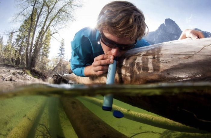 A model drinking from a stream using the Lifestraw.